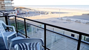 Un balcón con vista a la playa, sillas de plástico blancas y un edificio con balcón.