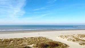 Une plage avec un phare visible au loin, des dunes de sable et un ciel dégagé.