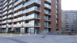 Un edificio residenziale moderno a più piani con balconi, un cortile pavimentato e cielo sereno.