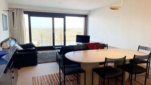 Una moderna camera d'albergo con un'ampia finestra, un tavolo da pranzo con sedie, un divano, una TV e un televisore a schermo piatto su un supporto.