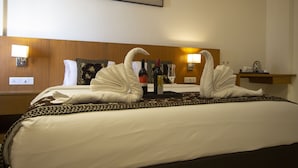 A hotel room with a neatly made bed, two swan-shaped towels, a wine bottle, and a glass on the bed. - Monarch Express (Rajgurunagar)