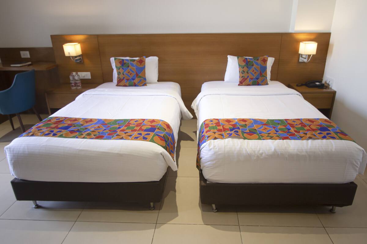 Duas camas de solteiro com cabeceiras de madeira, roupa de cama branca e cobertores coloridos com padrões geométricos.
