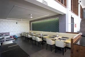 A family section of a restaurant with booths and tables, a green cushioned wall, and a staircase. - Monarch Express (Rajgurunagar)