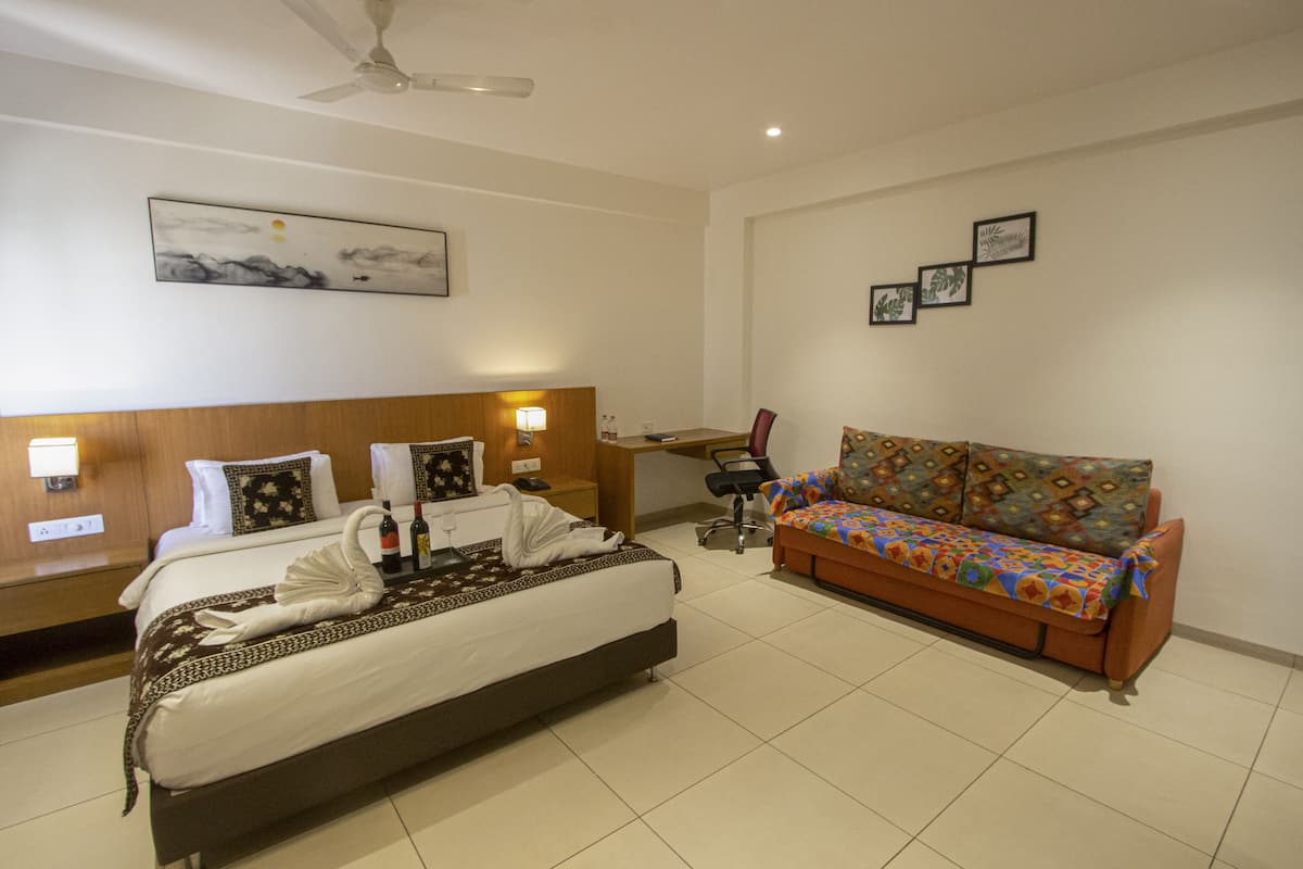 Quarto de hotel com cama, sofá, escrivaninha e ventoinha no teto.