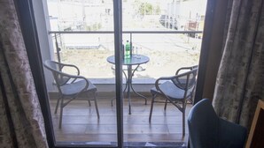 A room with a large sliding glass door leading to an outdoor area. Inside, there is a round table with two chairs and a bottle of Sprite. - Monarch Express (Rajgurunagar)