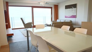 Un hotel moderno con una amplia mesa de vidrio, asientos cómodos, un sofá y vistas al mar a través de grandes ventanales.