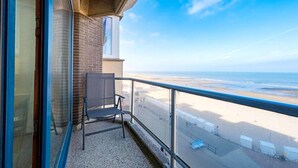 A balcony with a chair, a view of the beach, and a clear sky. - Nieuwpoort Beachfront Comfort (Nieuwpoort)