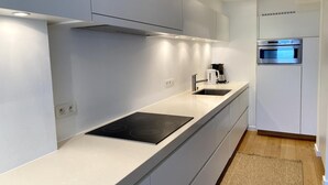A modern kitchen with white cabinetry, a black induction cooktop, a stainless steel oven, and a built-in sink. - Nieuwpoort Beachfront Comfort (Nieuwpoort)