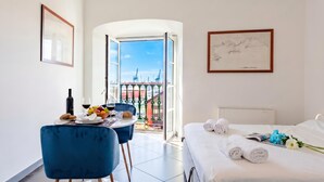 A hotel room with a bed, a dining table with chairs, a balcony with a view of cranes, and framed artwork on the walls. - Sea View Apartment Next To Acquarium (Genoa)