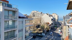 Una calle urbana moderna con edificios de varios pisos, un paso de peatones y coches aparcados.
