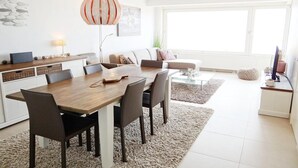 Een moderne woonkamer met een eethoek, grote ramen en een keuken.