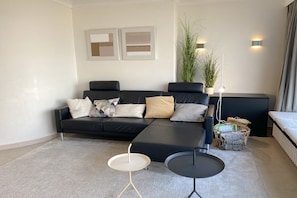 Uma sala de estar moderna com um sofá preto, uma mesa redonda pequena, um abajur e uma planta em vaso.