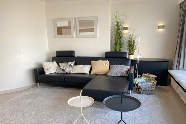 A modern living room with a black sofa, a small round table, a floor lamp, and a potted plant. - Picturesque apartment in Nieuwpoort (Nieuwpoort)