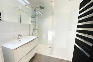 A modern bathroom with a glass-enclosed shower, a white sink, and a mirror above it.