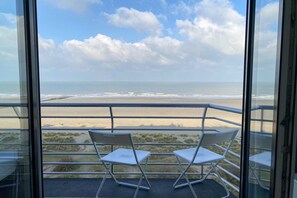 A balcony with two white chairs, a glass railing, and a view of the beach and ocean.