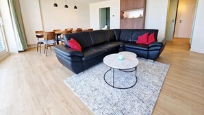 A modern living room with a black leather sofa, a round coffee table, and a dining area with wooden chairs and a table.