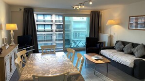A modern living room with a dining table, sofa, TV, and large sliding glass doors to a balcony. - Apartment in Nieuwpoort near Sandy Beaches (Nieuwpoort)