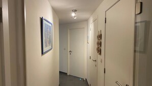 A hallway with a framed picture on the left wall, a door at the end, and a light fixture on the ceiling. - Apartment in Nieuwpoort near Sandy Beaches (Nieuwpoort)