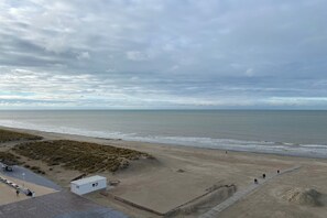 A beach with a sandy path, a small white building, and the ocean in the background.