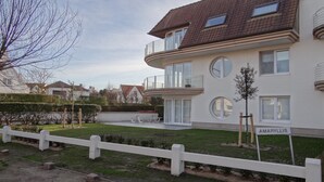 Ein zweistöckiges Wohngebäude mit Balkon, kleinem Garten und weißem Zaun.