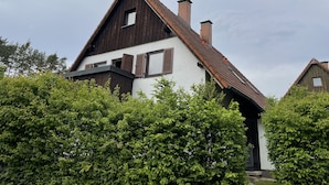 Uma casa tradicional com telhado inclinado, fachada de madeira e várias chaminés.