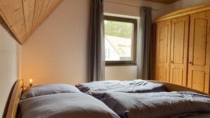 Quarto com duas camas, janela com cortinas, guarda-roupa de madeira e teto inclinado.