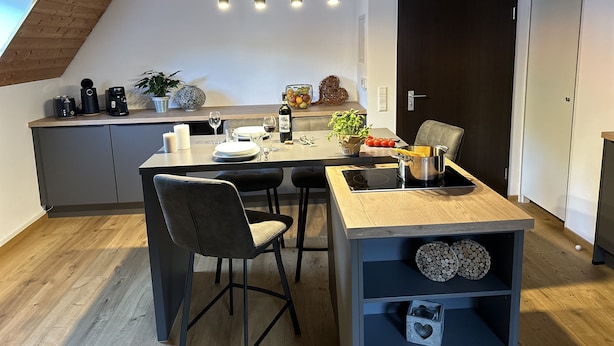 Cozinha moderna com área de jantar, apresentando teto de madeira, porta preta e mesa de jantar com cadeiras.