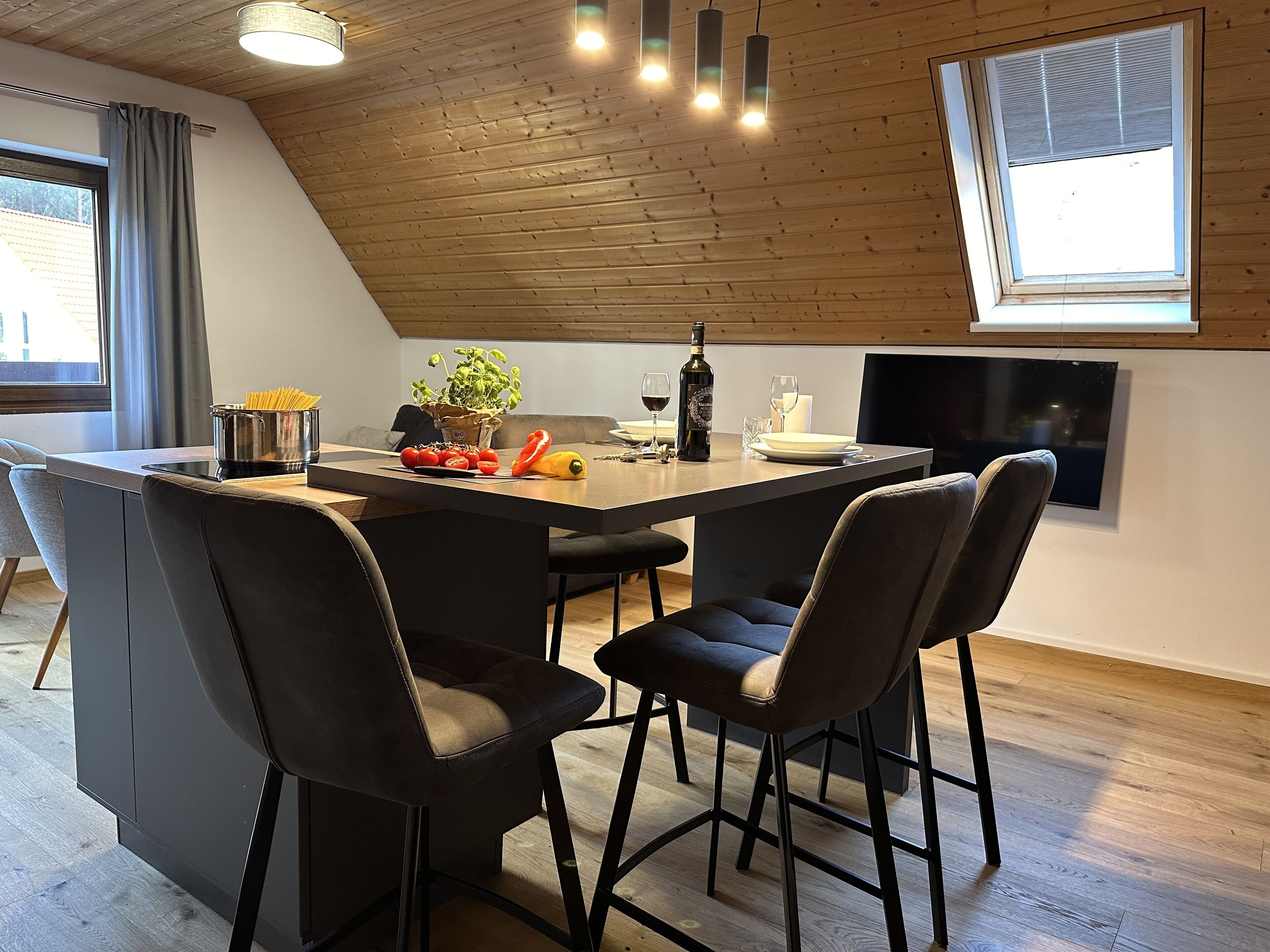 A modern dining area with a wooden ceiling, a large window, and a flat-screen TV mounted on the wall.