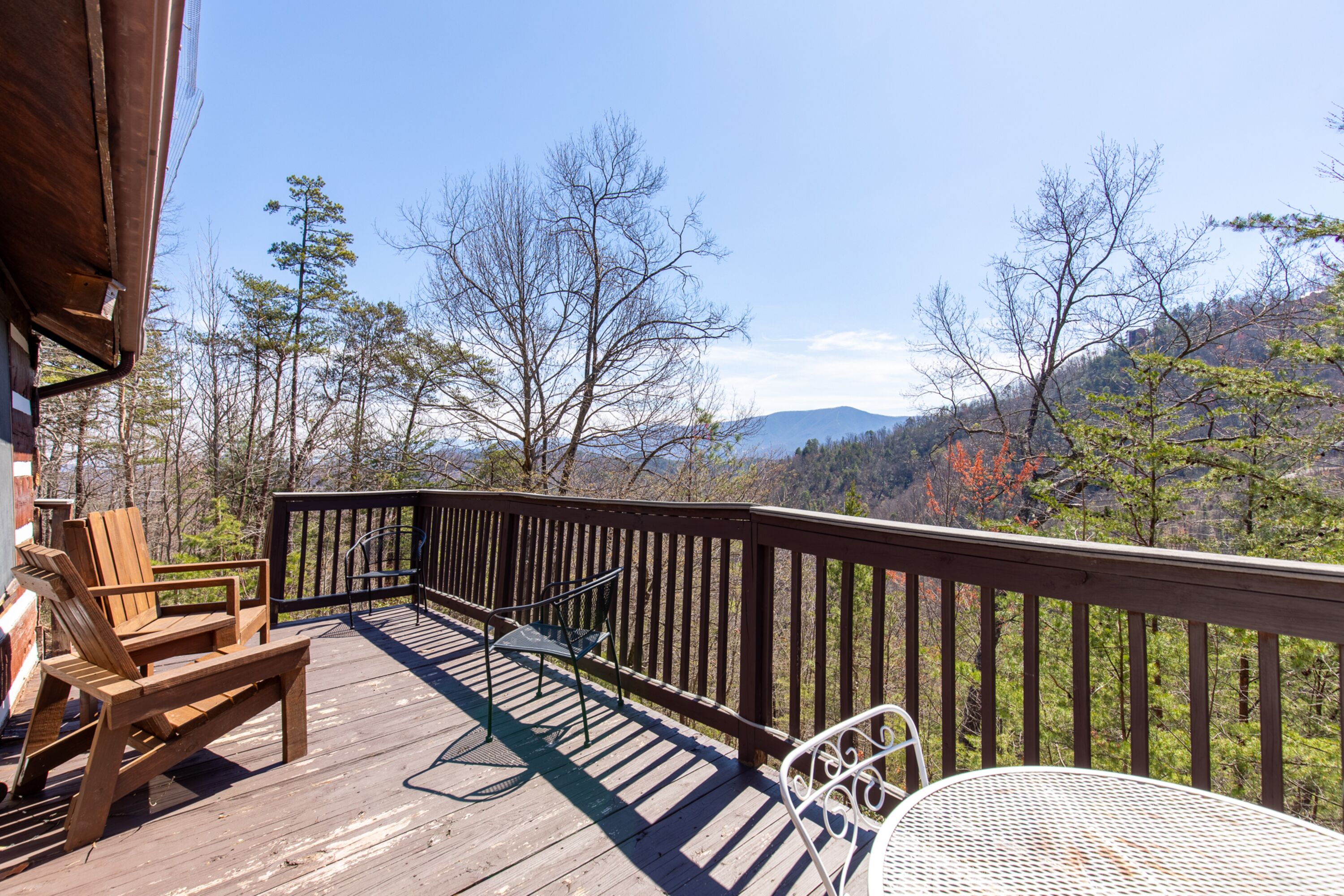 A wooden deck with outdoor furniture, including a chair and a table, overlooking a mountainous landscape.
