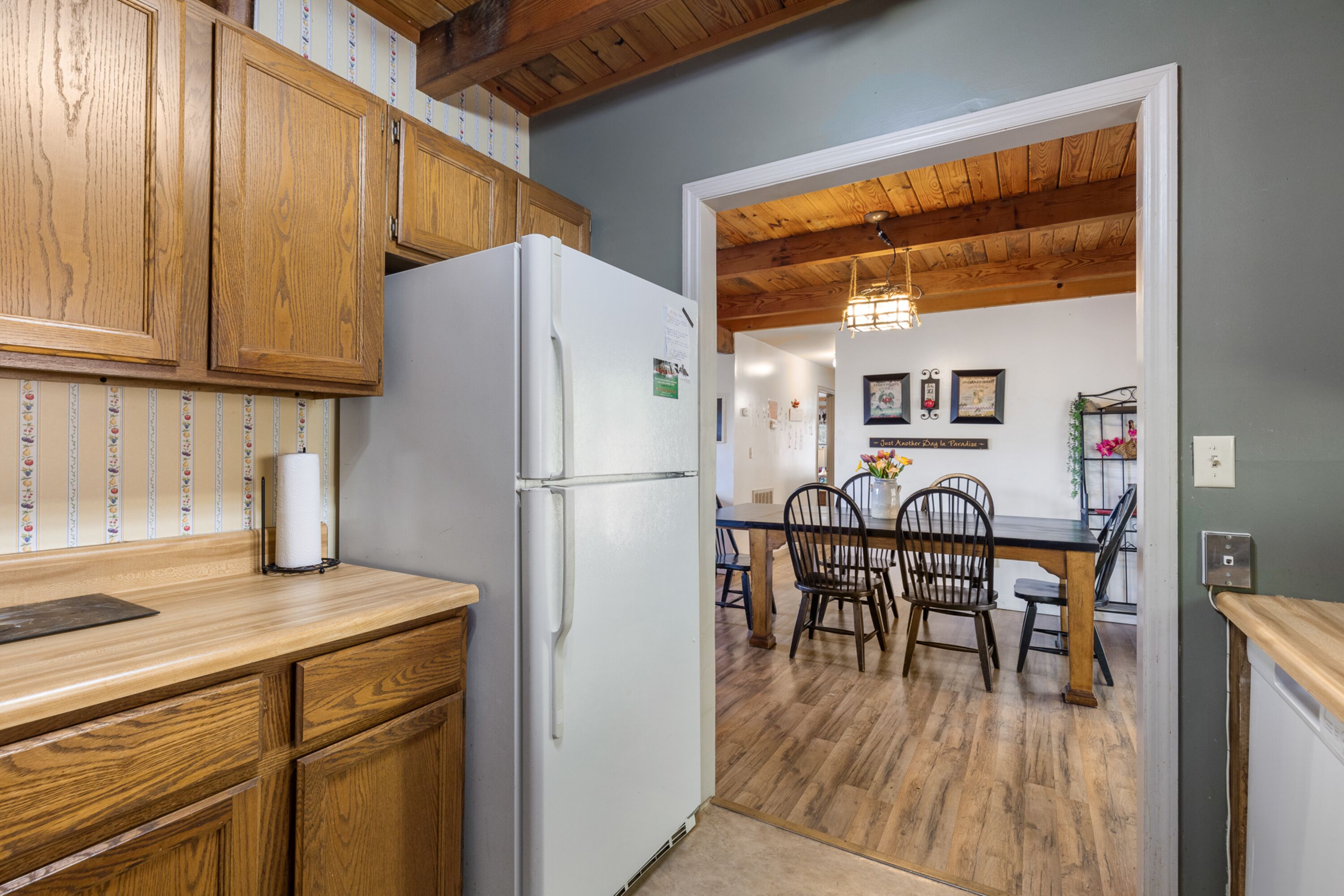A kitchen with wooden cabinets, a white refrigerator, and a dining area with wooden chairs and a table.