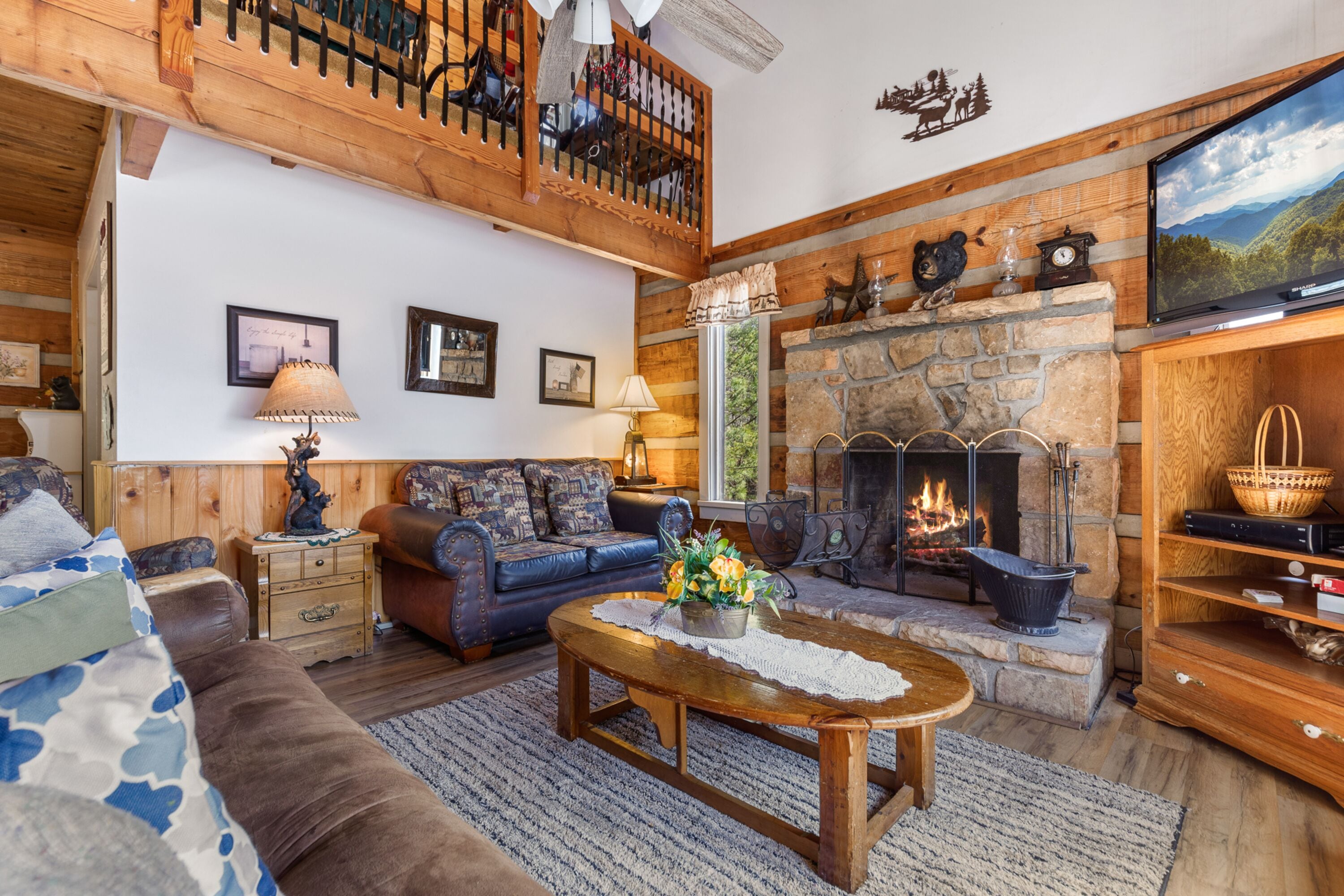 A cozy living room with a stone fireplace, a wooden ceiling, and a large flat-screen TV.