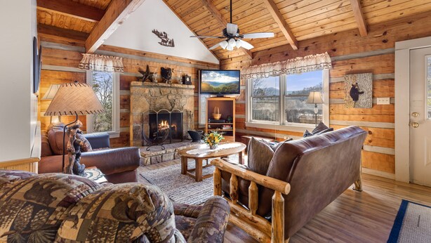 A log cabin interior with a fireplace, leather furniture, and a stone wall. - Mountain Vintage (Sevierville)