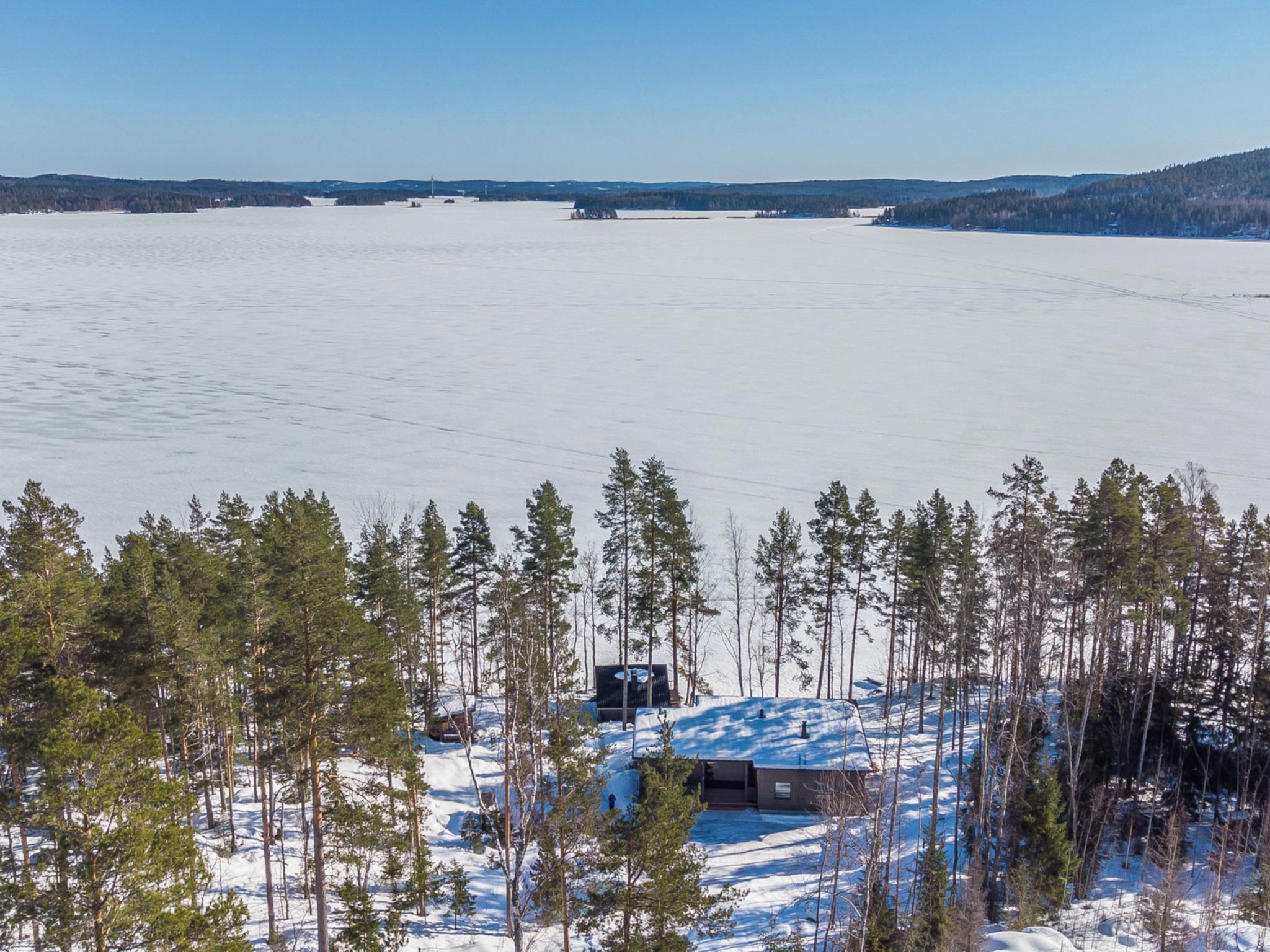 A cabin surrounded by a forest with a frozen lake in the background.