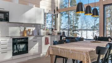 A modern kitchen with white cabinetry, a dining area with a striped tablecloth, and large windows offering a view of trees.