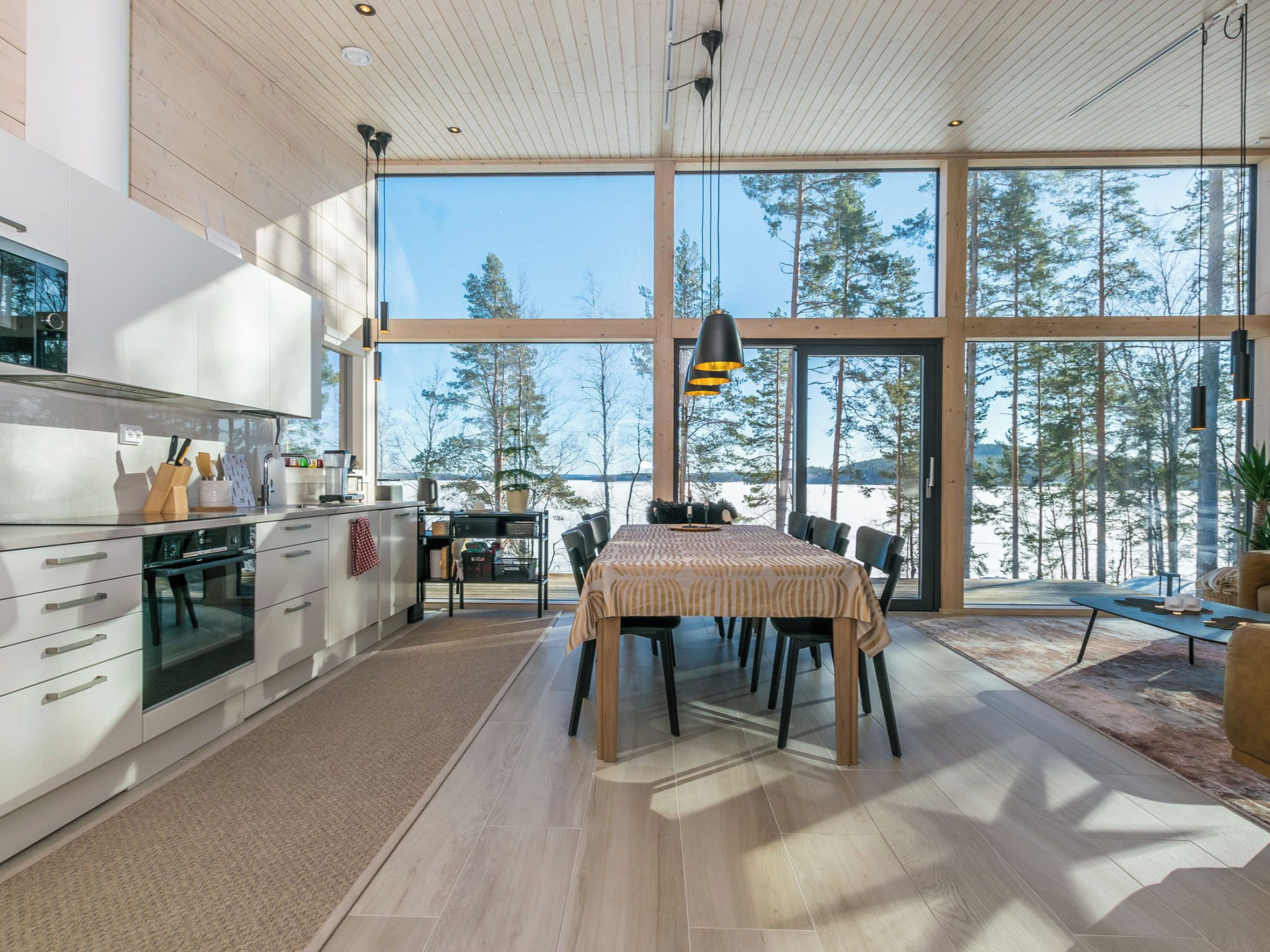 Une cuisine moderne dotée de grandes fenêtres, un coin repas avec une table et une vue sur les arbres.