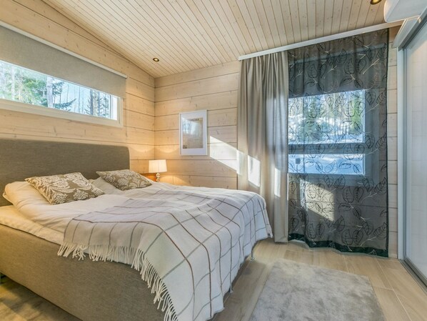 A bedroom with a bed, a nightstand, a lamp, a framed picture, and a window with curtains.