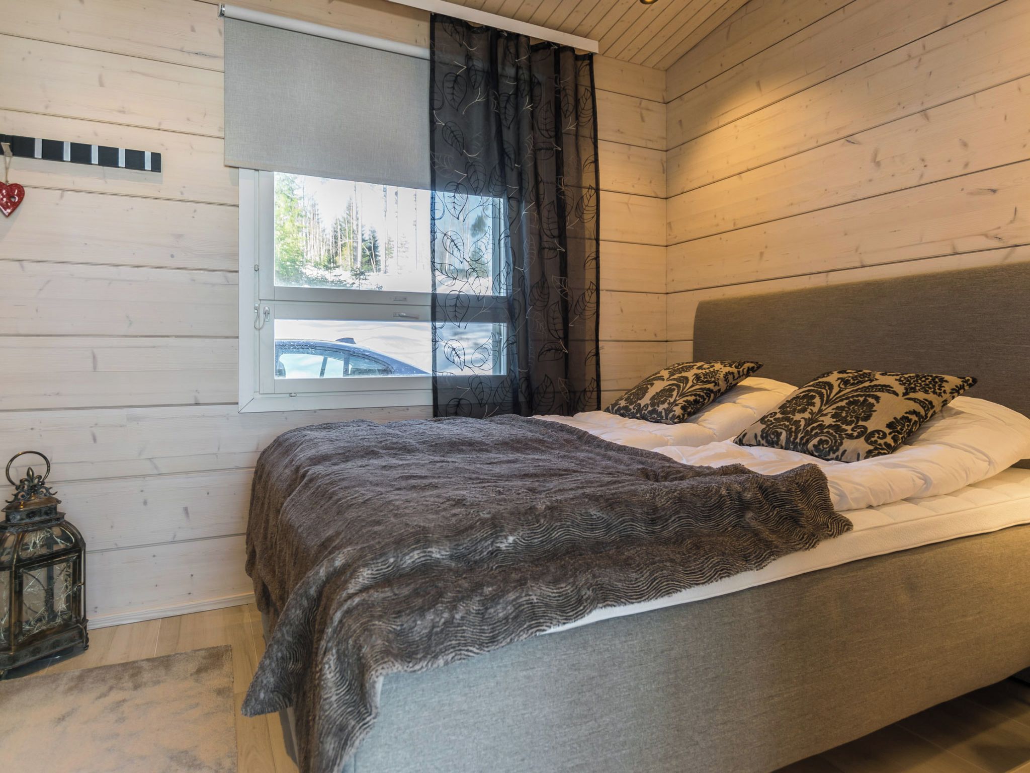 Une chambre à coucher avec un lit, une fenêtre avec des rideaux, une lanterne et une horloge fixée au mur.
