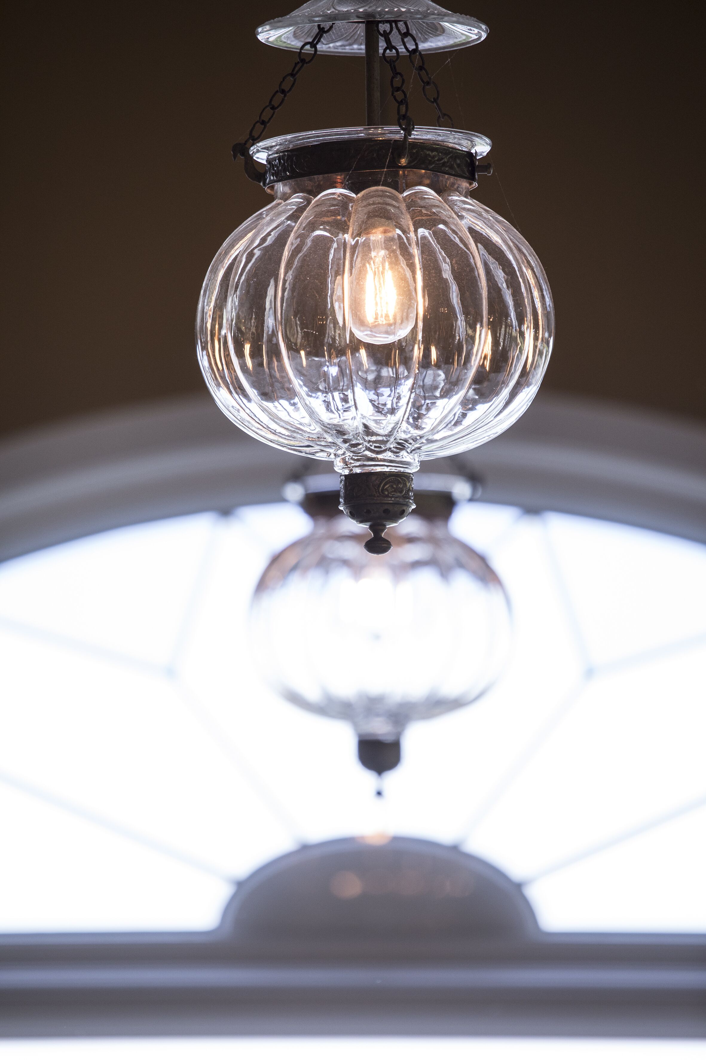 A clear glass chandelier with a visible light bulb, hanging from a ceiling with a chain.