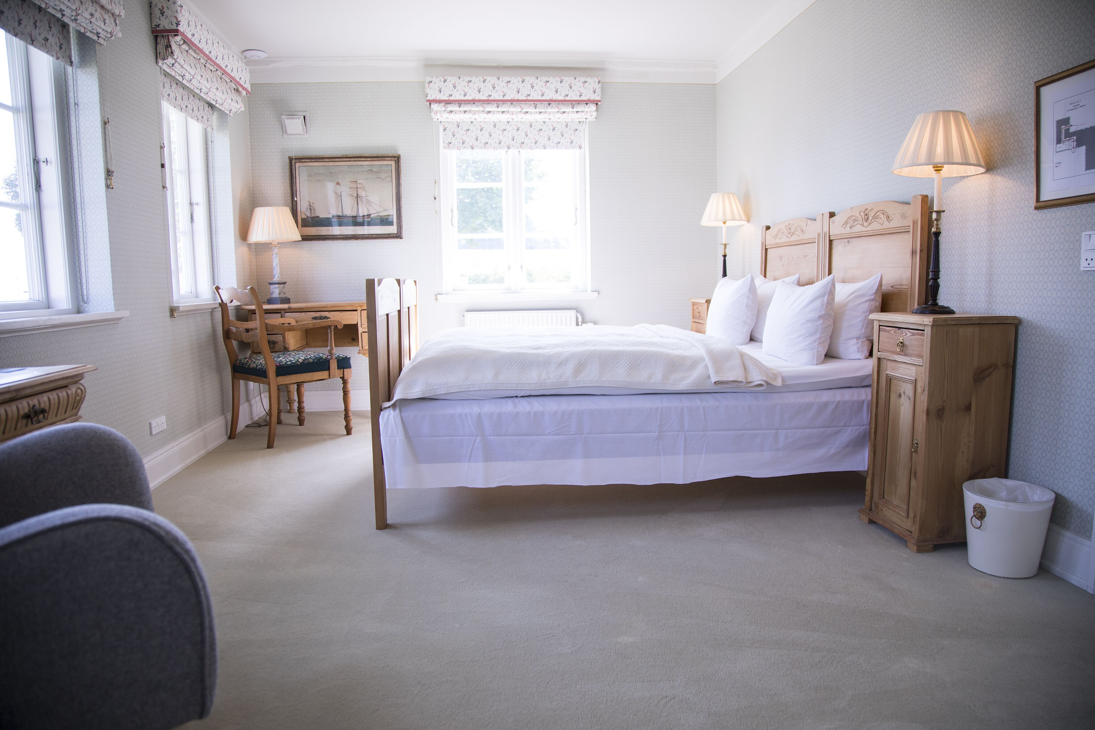 A bedroom with a bed, bedside tables, a chair, a desk, and a window with curtains.