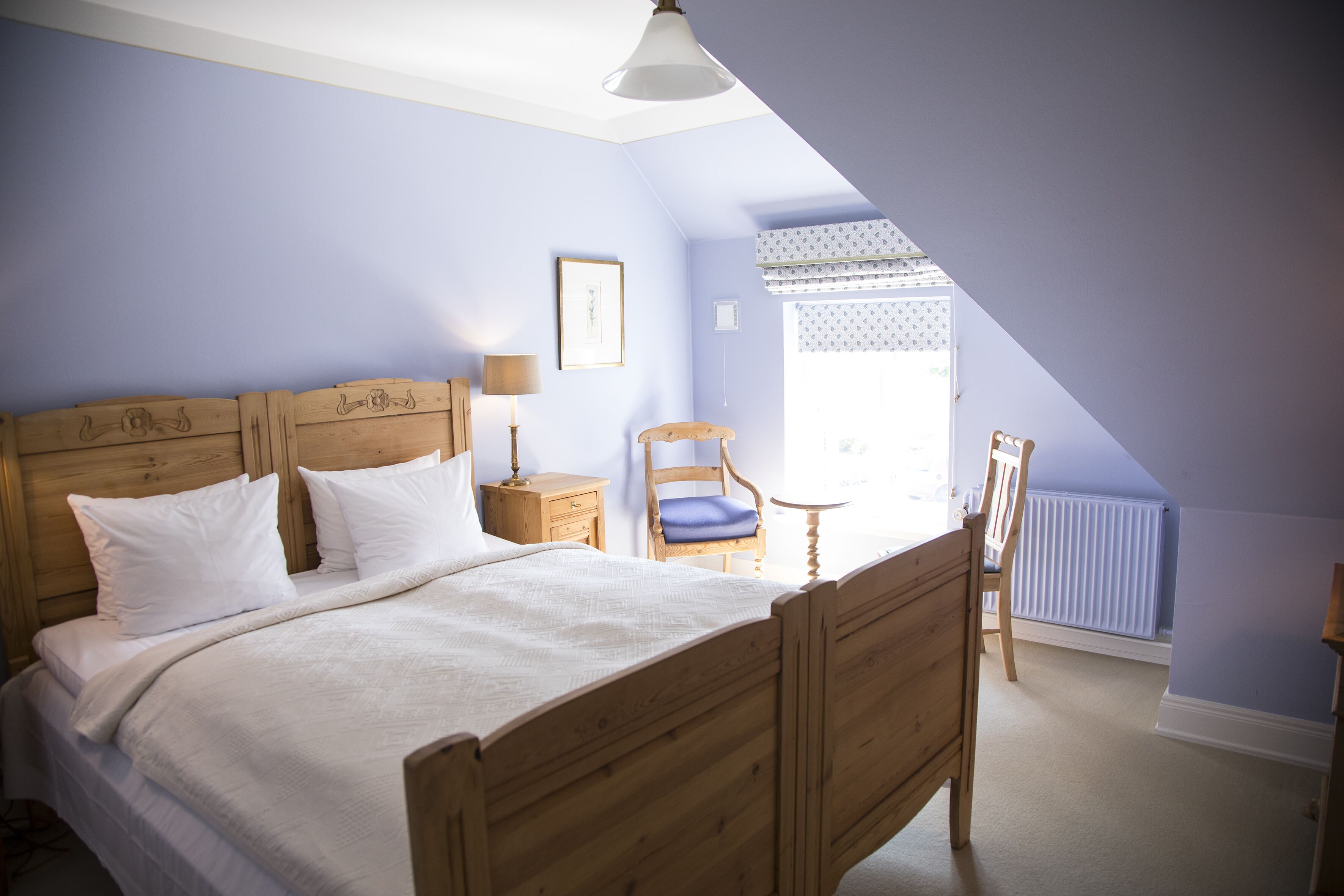 Un dormitorio con una cama de madera, una mesita de noche, una silla, una ventana con persianas y un radiador.