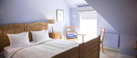 Un dormitorio con una cama de madera, una mesita de noche, una silla, una ventana con persianas y un radiador.