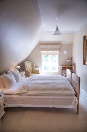 A bedroom with a large bed, a chair, a desk, and a window with curtains.
