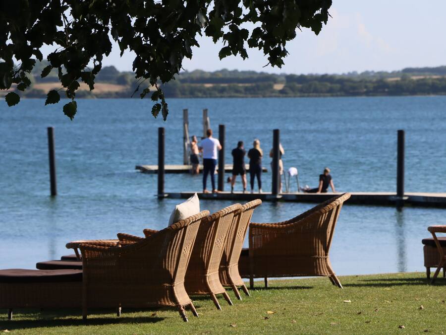 Wicker furniture on a grassy area by a lake, with a dock in the background where people are present.