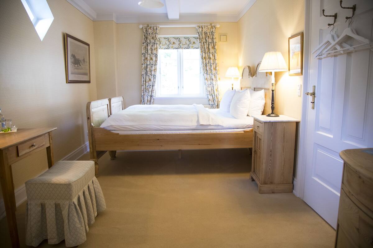 Ein Schlafzimmer mit Bett, Nachttischen, einer Bank, einem Kleiderschrank und einem Fenster mit Vorhängen.