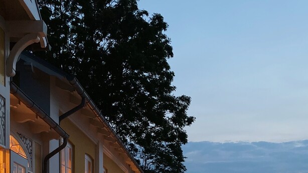An outdoor deck with wooden benches and tables, overlooking a body of water. - Ballebro Færgekro (Sønderborg)