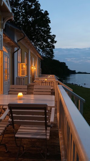 An outdoor deck with wooden benches and tables, overlooking a body of water.