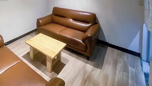 Quarto com sofá de couro marrom, mesa de centro de madeira e piso claro.