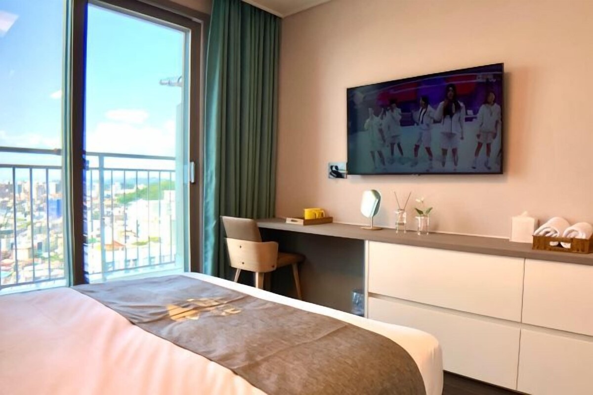 Habitación de hotel con cama, escritorio, una silla, un cuadro y vistas a la ciudad.