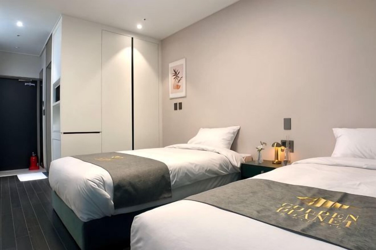 Habitación de hotel con dos camas, un armario, una mesita con una lámpara y una obra de arte colgada en la pared.