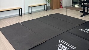 Un gimnasio con colchonetas negras, bancos de madera, un espejo, una puerta y plantas colgantes.